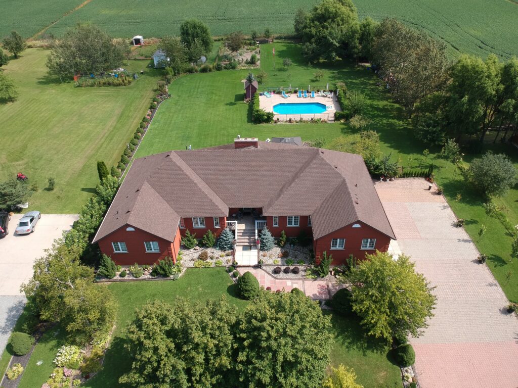 Large brick home with a new brown shingle roof and backyard pool in a rural setting